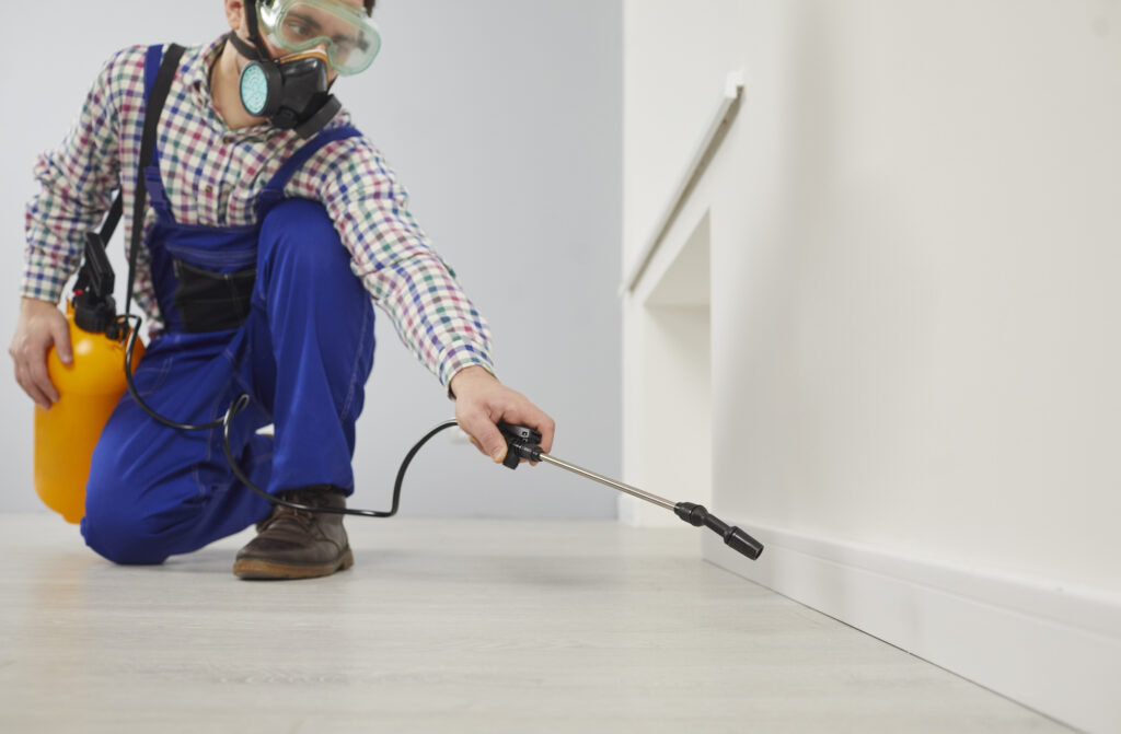 GettyImages 2193273746 A pest control worker spraying pesticide along the indoor baseboard.